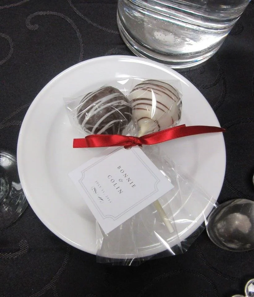 Two chocolate and vanilla truffles with white and milk chocolate drizzles, wrapped in clear plastic and tied with a red ribbon.
