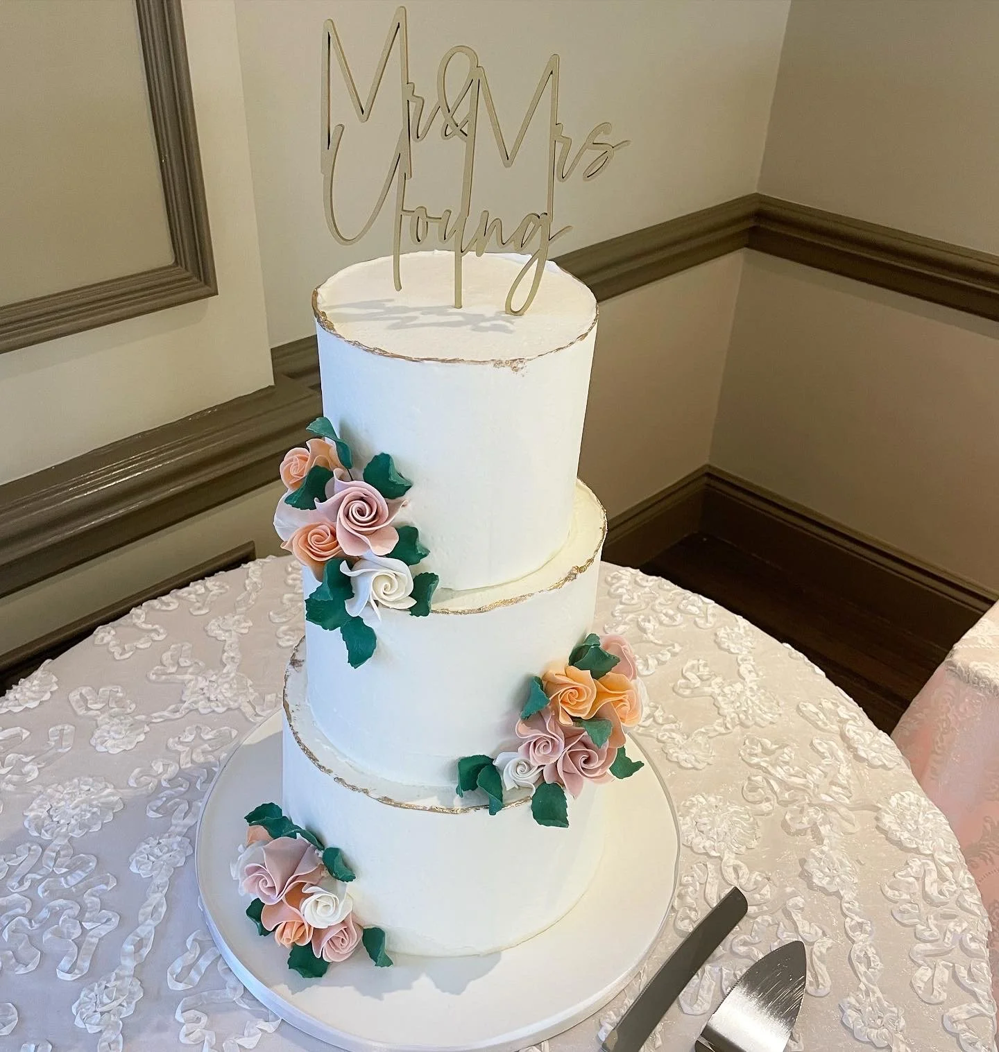 Three-tier white wedding cake decorated with pink and white sugar roses and green leaves.