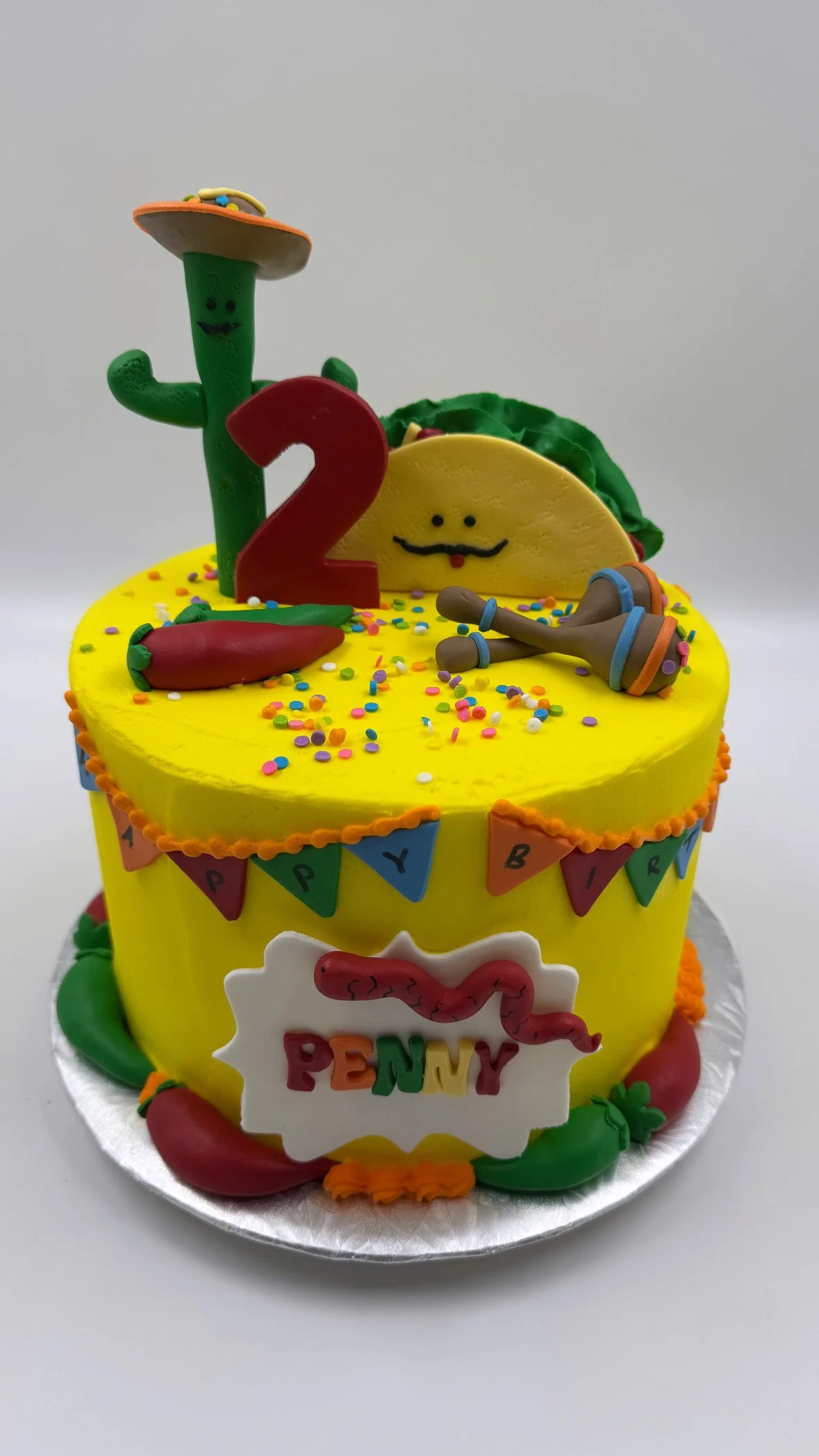 Colorful birthday cake decorated with peppers, chili peppers, and festive banners and various playful decorations.