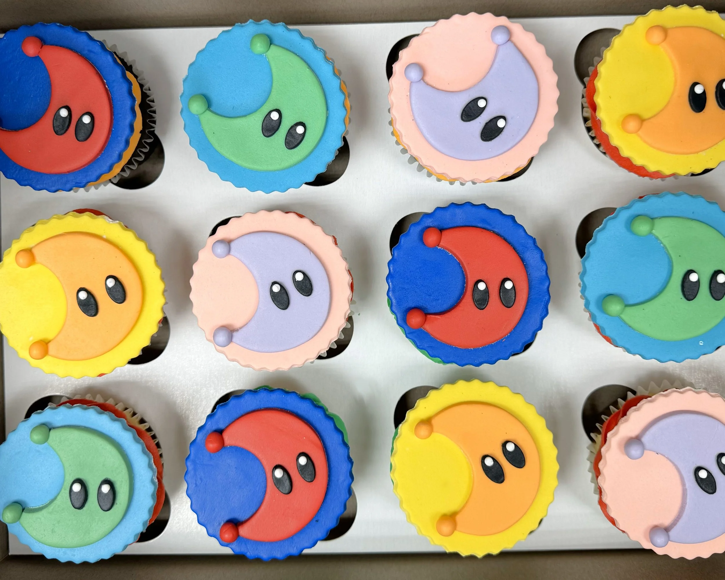 Colorful cupcakes with moon and star designs, arranged in a grid, with each cupcake decorated with icing and small spherical embellishments.