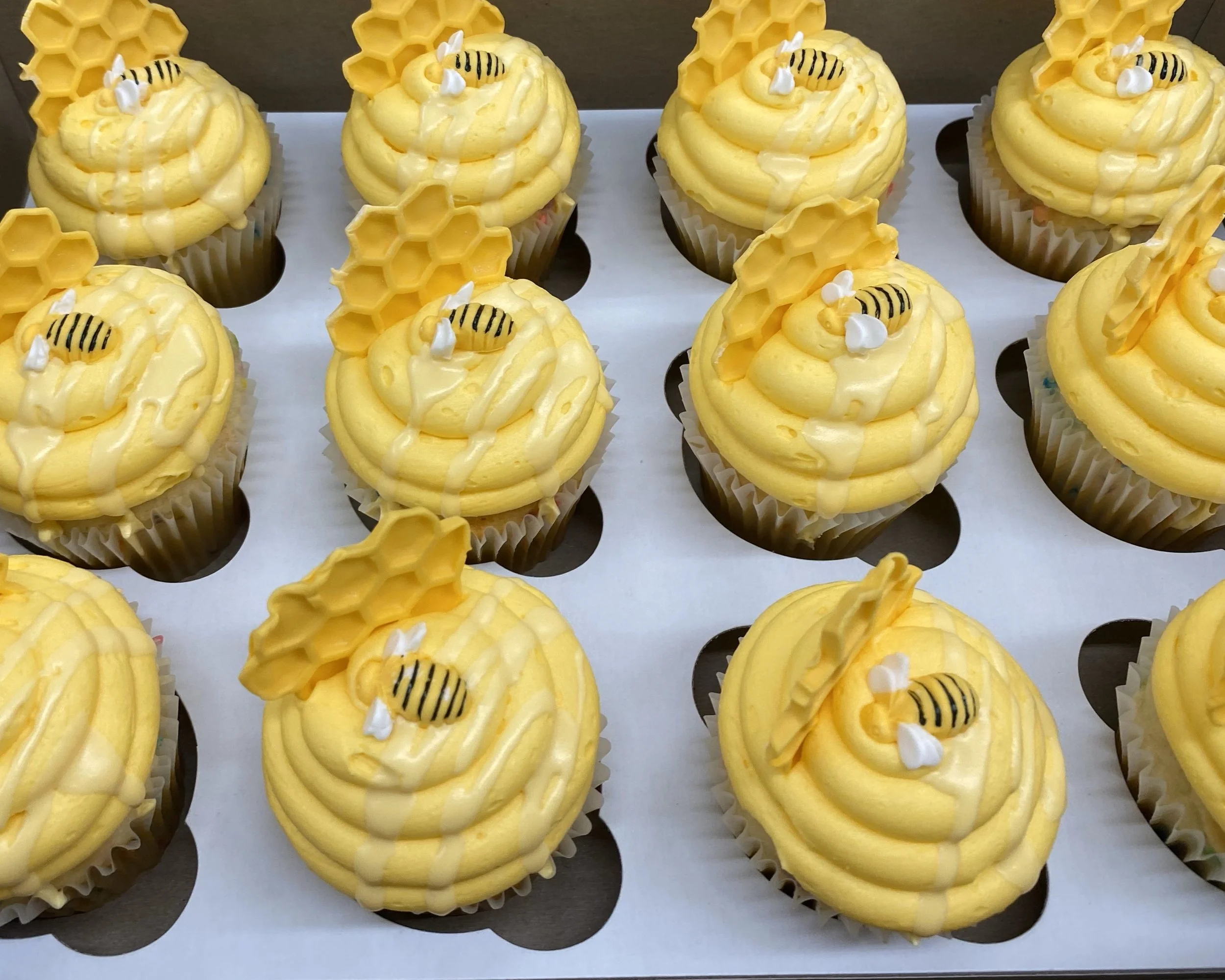 Yellow cupcakes decorated with honeycomb and bee toppers, drizzled with honey