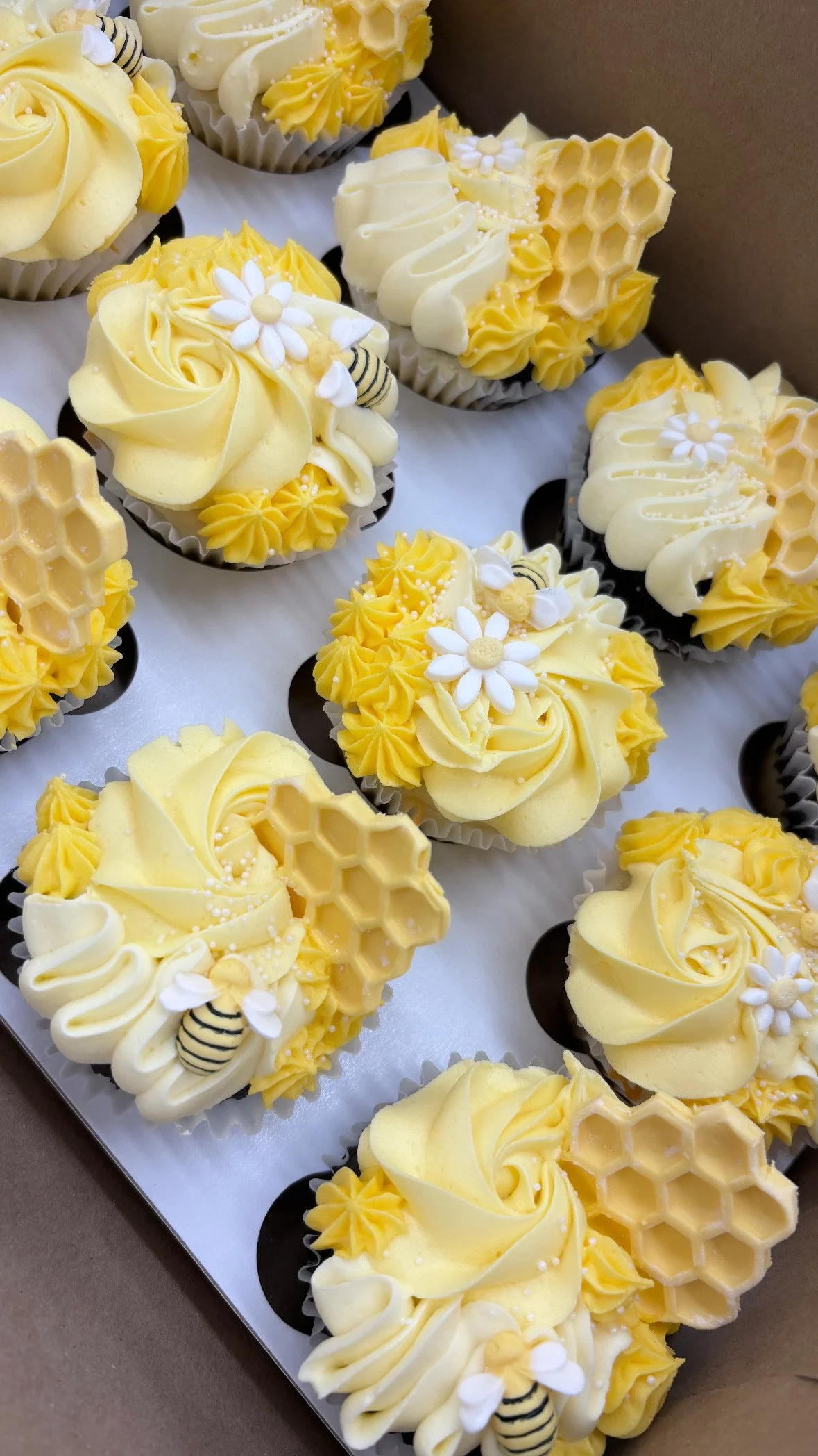 Yellow and white decorated cupcakes with honeycomb and bee embellishments.