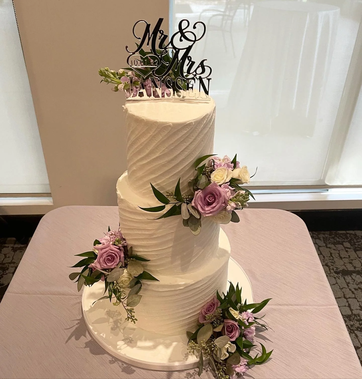 Three-tiered wedding cake decorated with pink and white roses, green leaves.