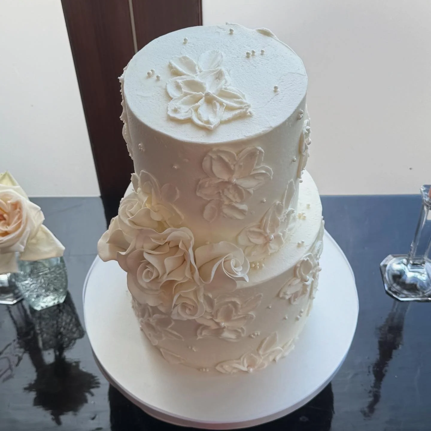 Three-tiered white wedding cake with floral icing decorations placed on a white cake board.