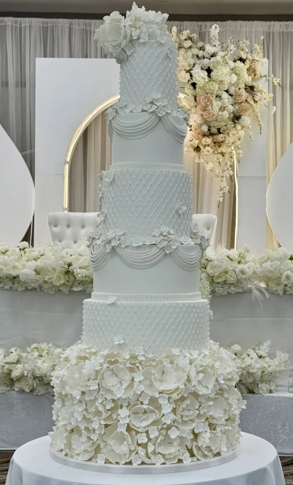 A tall, multi-tiered white wedding cake with floral and scroll decorations.