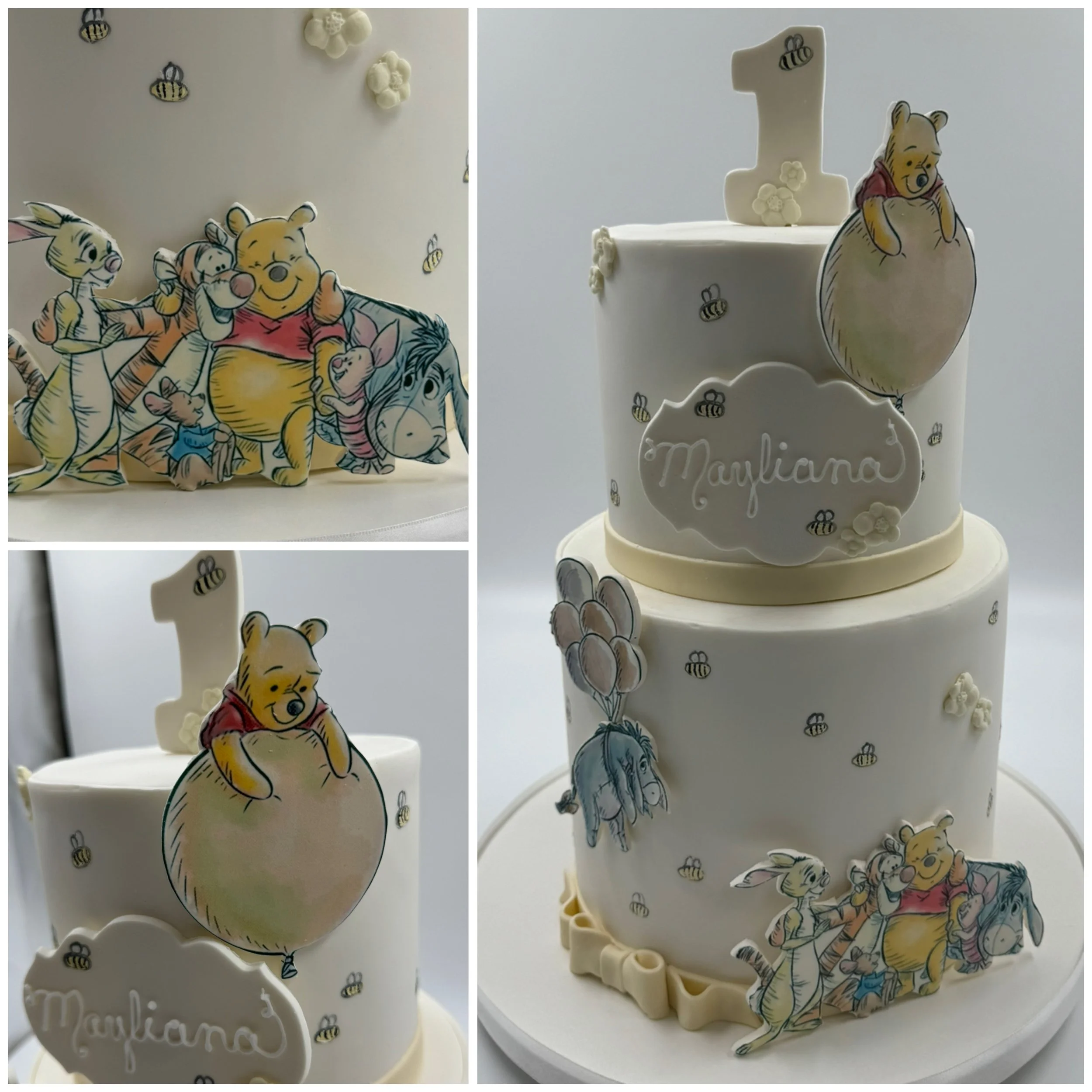 Two-tier birthday cake decorated with Winnie the Pooh characters and bees. The top tier features a large number one candle and a Pooh figure in a honey pot. The bottom tier has Winnie the Pooh, Piglet, Eeyore, and Rabbit cutouts, with a white plaque 