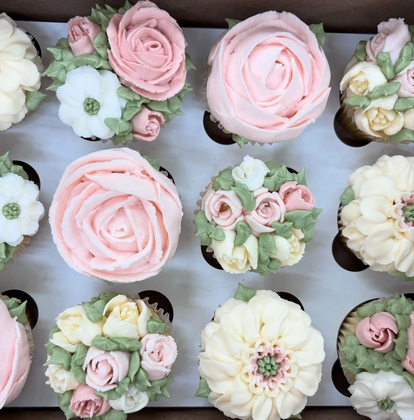 Decorative cupcakes with floral frosting designs in soft pink, white, and green colors arranged on a tray.