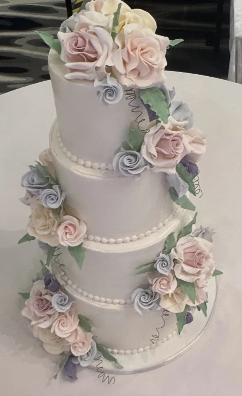 A three-tiered white wedding cake decorated with pastel-colored roses and green leaves.