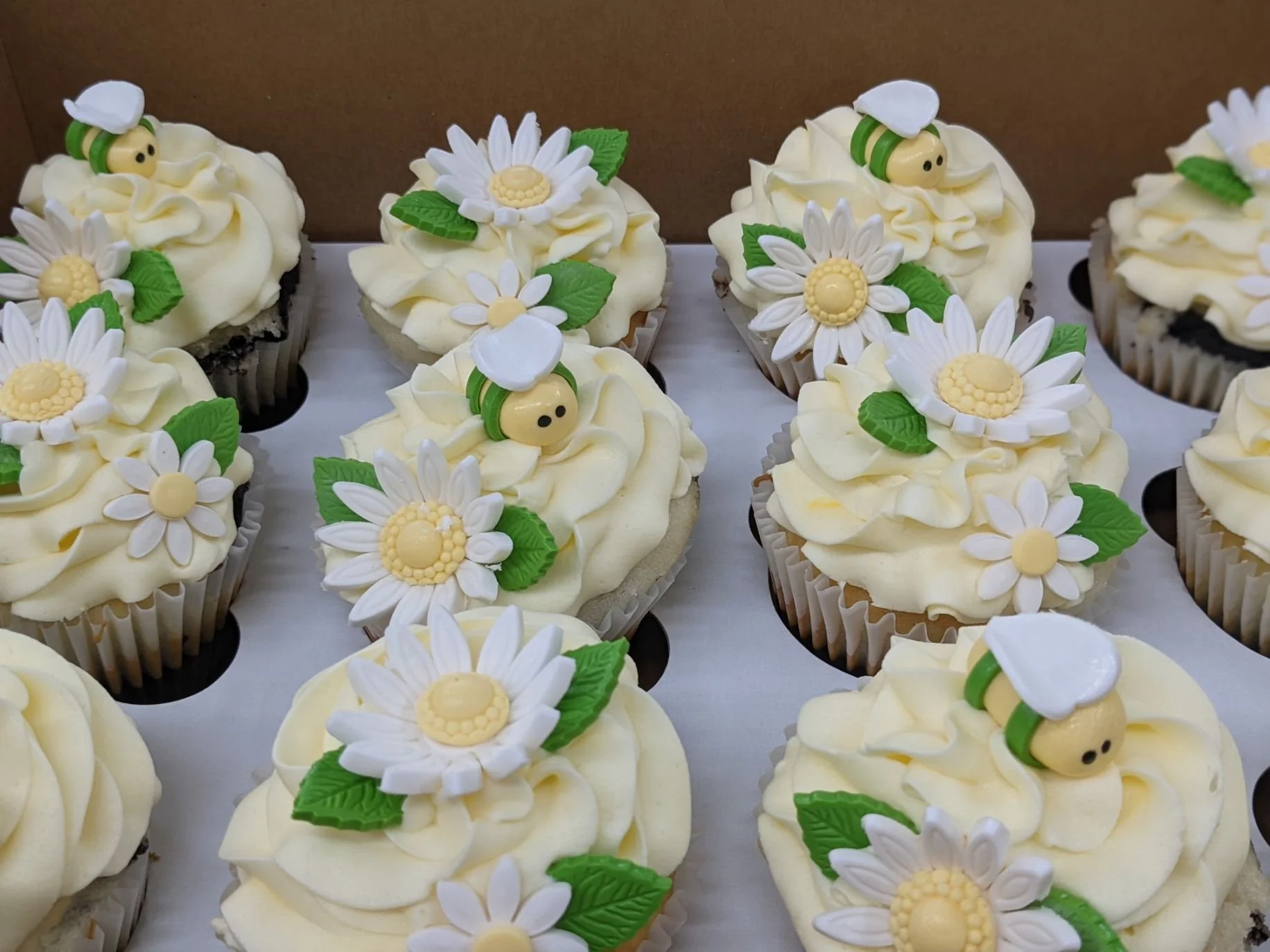 Cupcakes decorated with white and yellow flowers and small bee figurines on top.