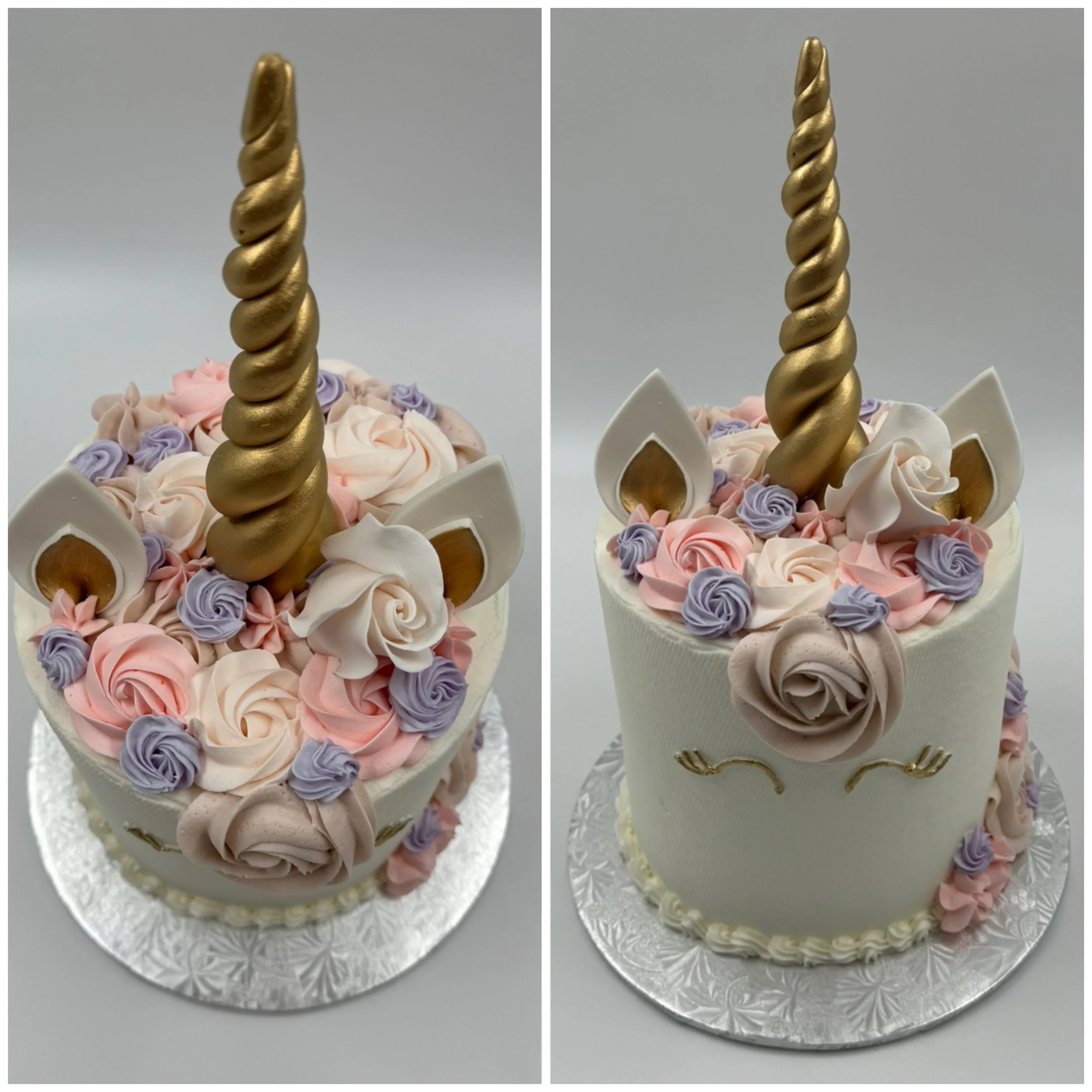 Unicorn-themed birthday cake decorated with pastel pink, purple, and cream buttercream flowers, a gold spiral unicorn horn, white ears with gold accents, and a simple face with closed eyes and a blush on a silver cake board.