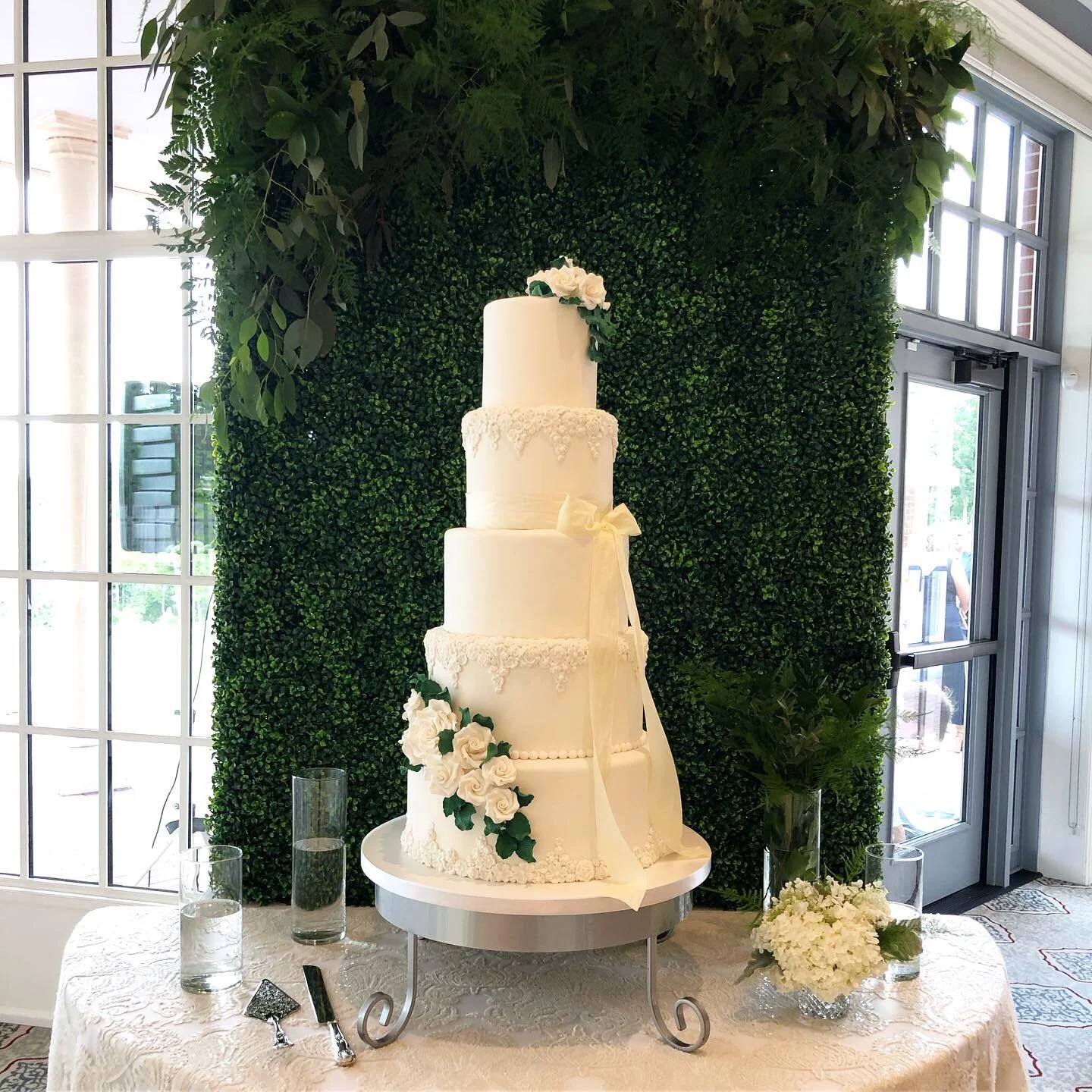 A white multi-tiered wedding cake decorated with white roses and greenery.