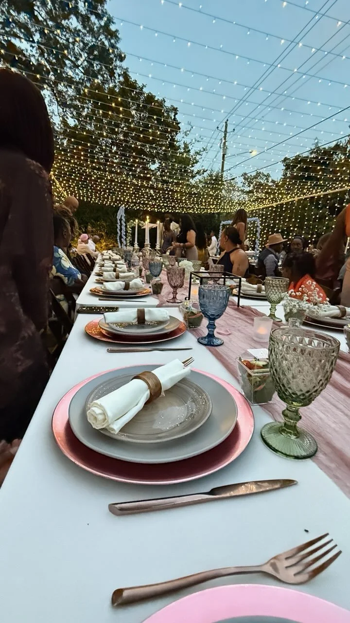 Set dinner table outdoors decorated with string lights and surrounded by guests.