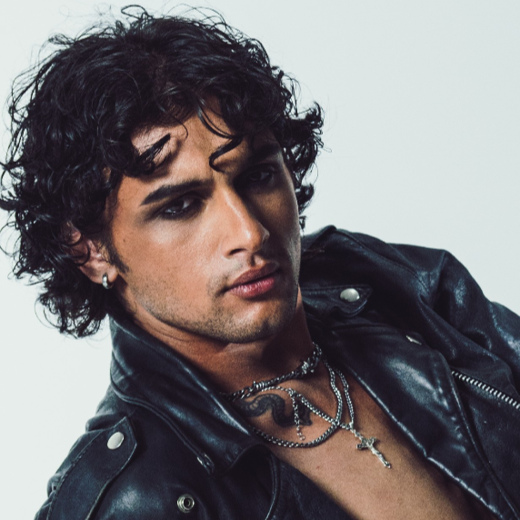 A young model and actor, Jett Williams, with curly dark hair wearing a black leather jacket and layered necklaces against a plain background.