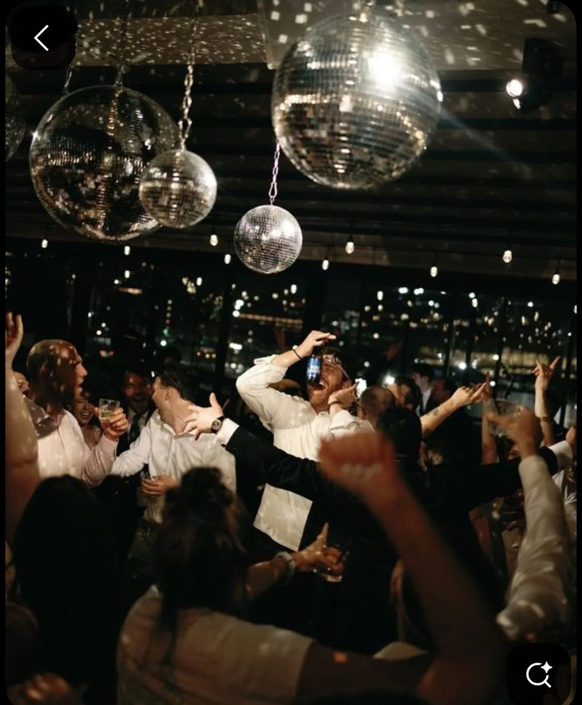 People dancing and celebrating at a party with disco balls hanging from the ceiling.