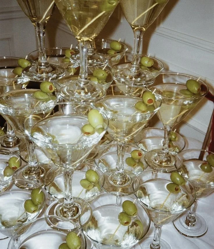 Multiple martini glasses filled with a clear drink, garnished with green olives on toothpicks.