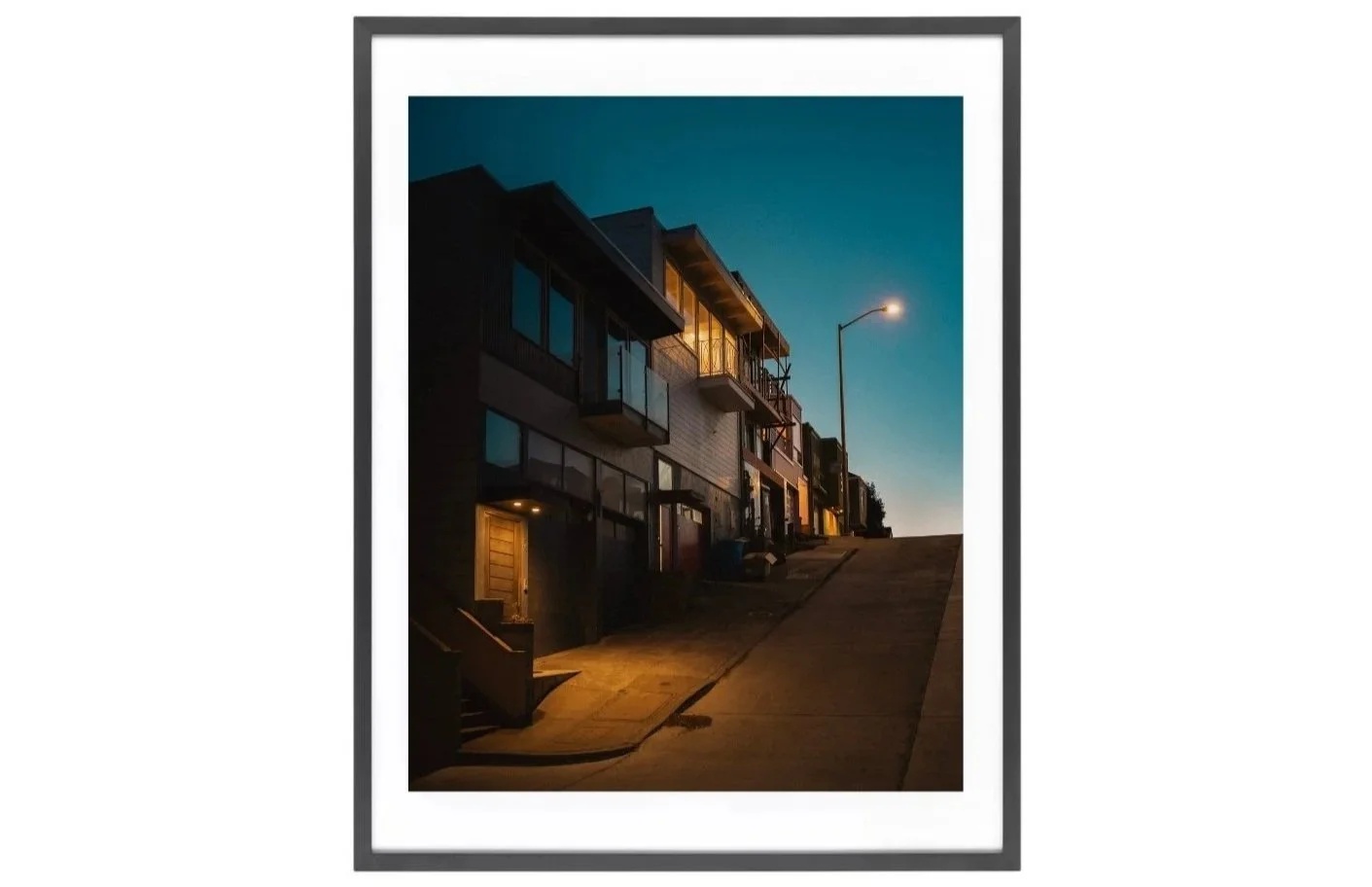 Night view of a Bernal Heights street with a row of houses and a glowing street lamp at the end.