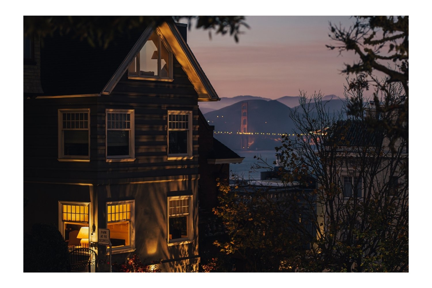 House, night, lamp in the window, Golden Gate Bridge in the background. 