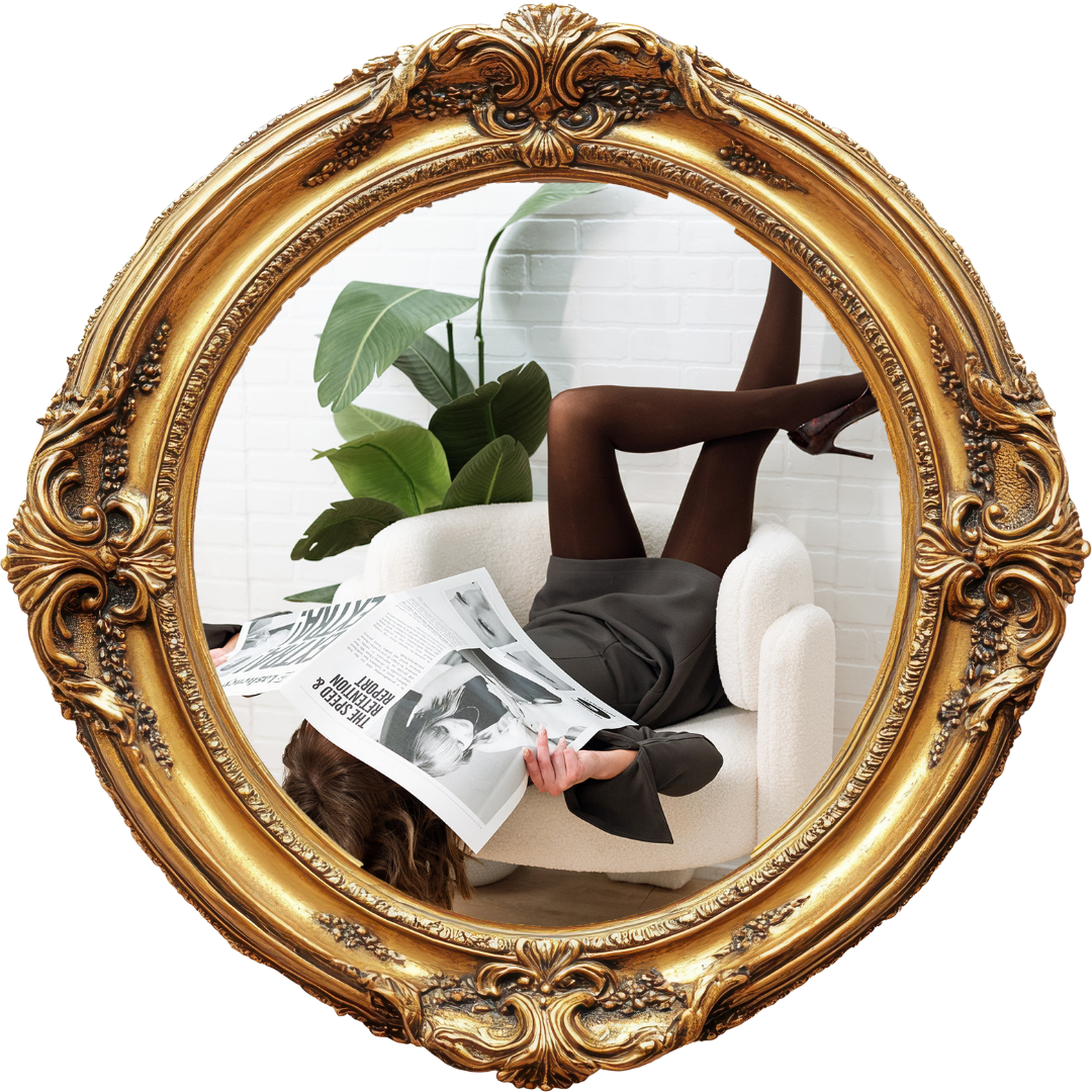 Person lying upside down on a white sofa, reading a newspaper, with legs up on the armrest, seen through an ornate gold mirror. There is a large green plant and a white brick wall in the background.