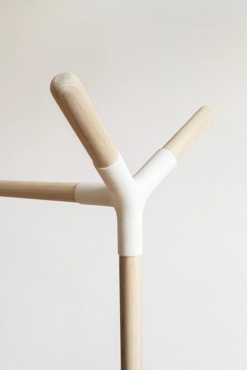 Close-up of a modern coat rack made of wooden sticks connected by white joints, with a plain white wall in the background.
