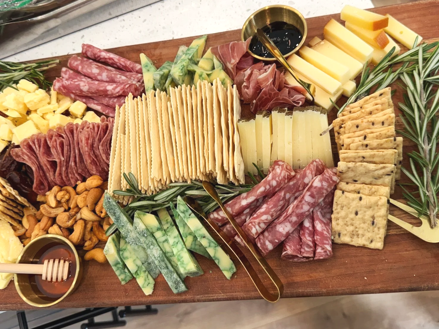 A cheese and charcuterie board with various cheeses, meats, crackers, nuts, and garnishes on a wooden serving tray.