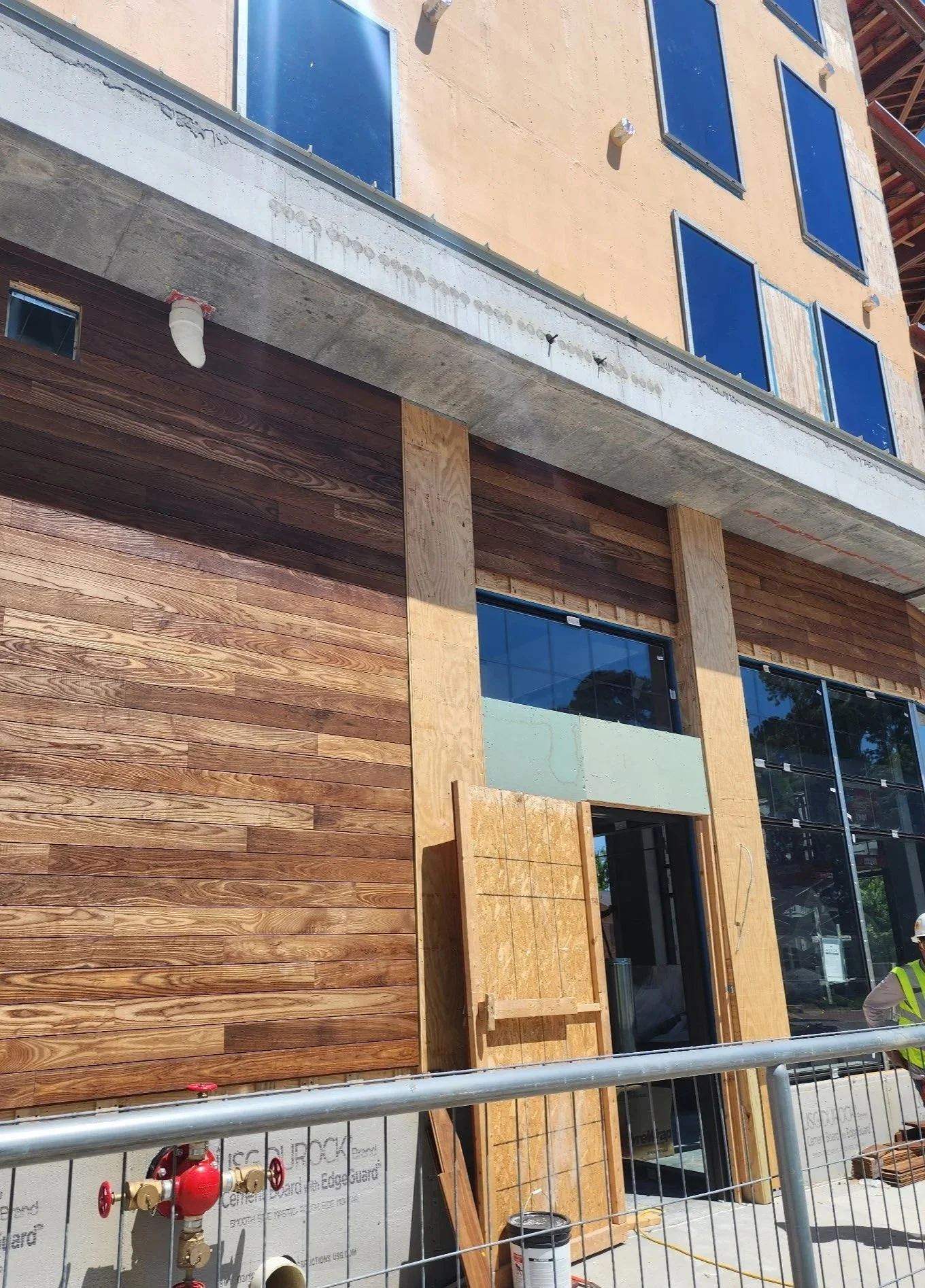 Construction site with a building under construction, featuring wooden and concrete exterior walls, windows, and construction workers.