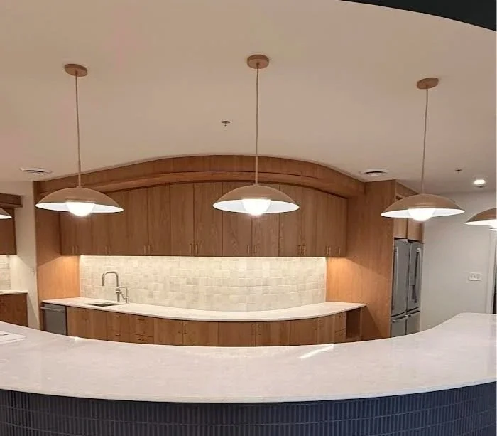 Modern kitchen with wooden cabinets, beige backsplash, white countertop, and three hanging pendant lights.