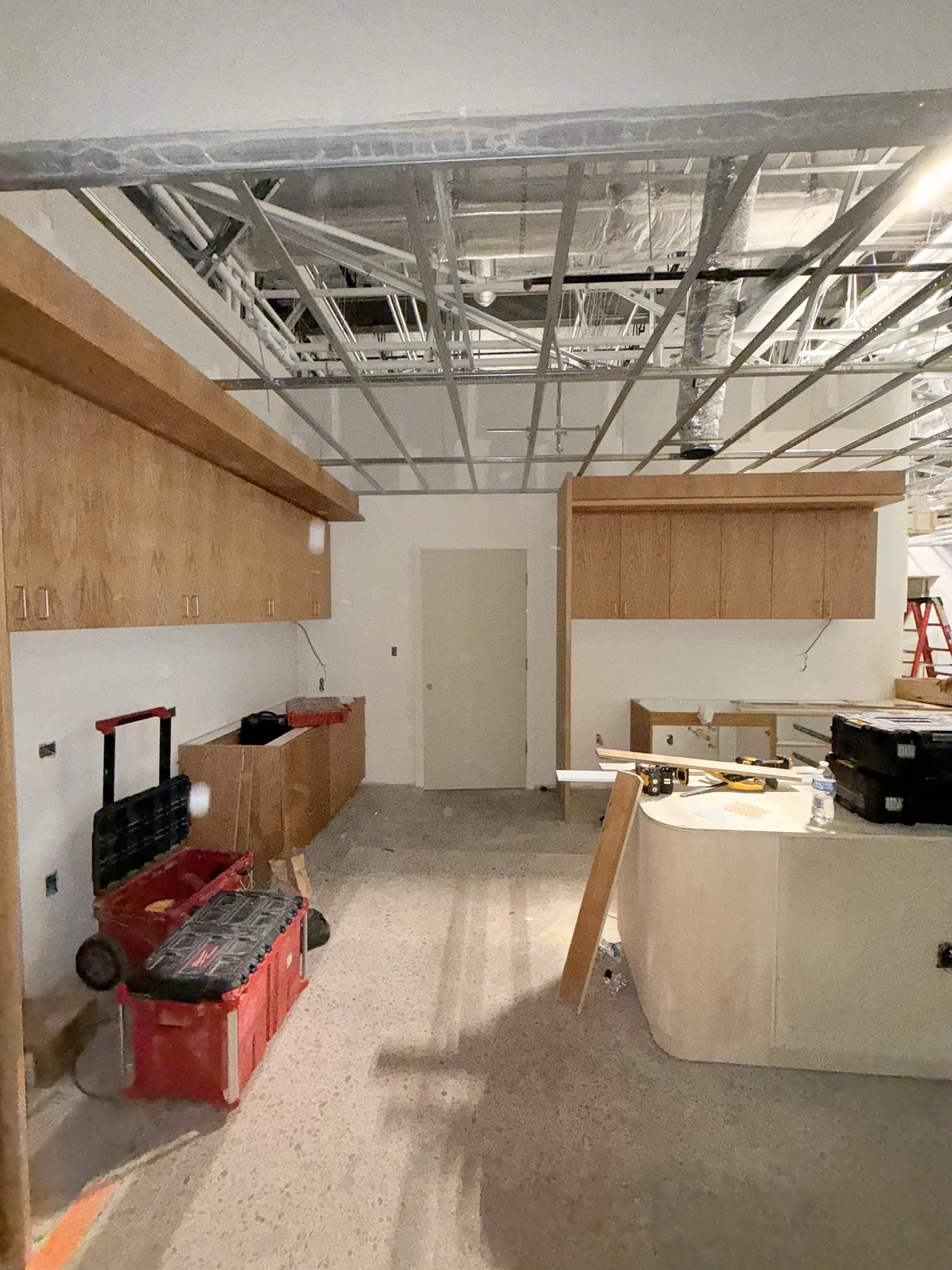 Construction site with wooden cabinets, tools, and construction equipment under a partially finished ceiling.
