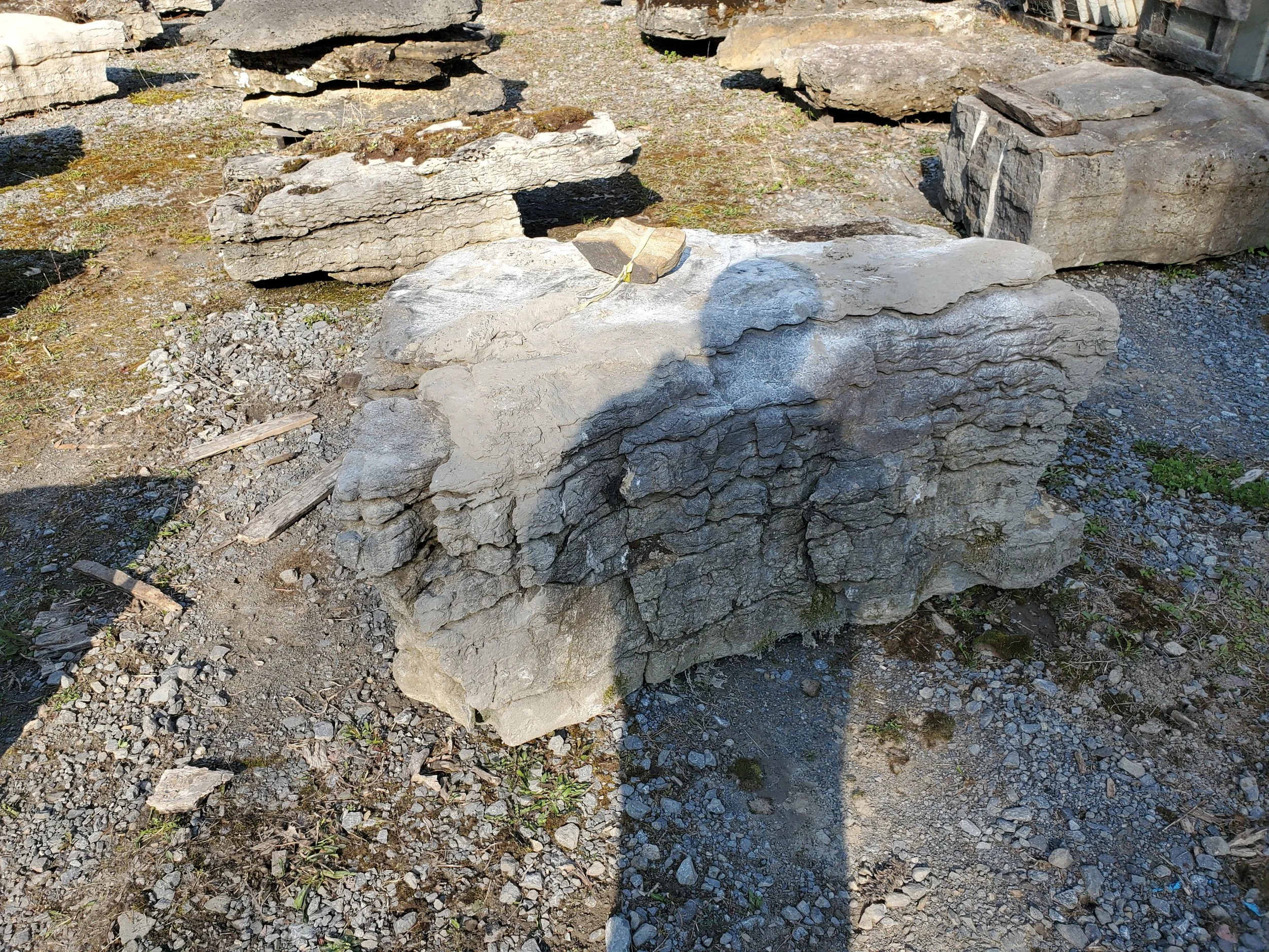Stack of irregularly shaped flat stones outdoors on dirt and gravel ground with other stone piles in the background.