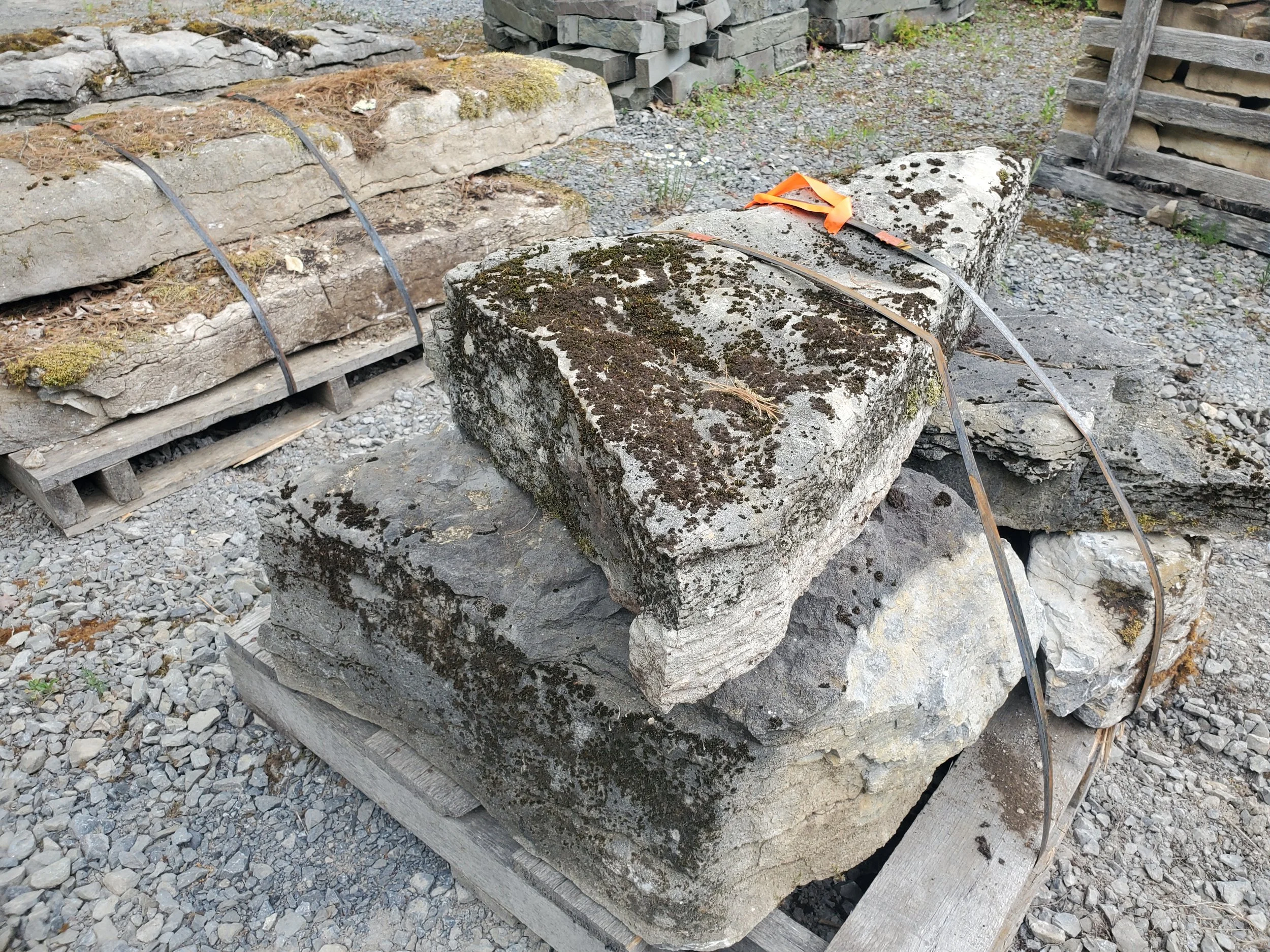 Stacked concrete and stone blocks with metal straps and wooden pallets outdoors.