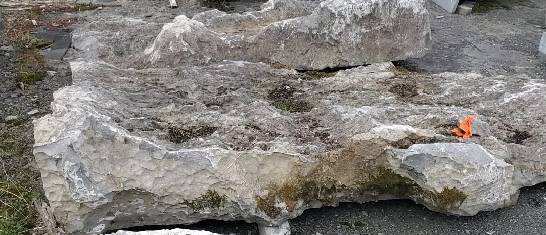 Large natural rock formation with rough, textured surface and patches of moss, located outdoors.