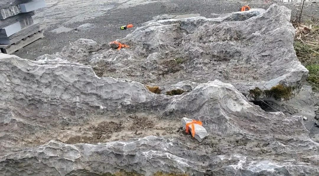 Large textured gray rocks on the ground with construction tools and straps visible.
