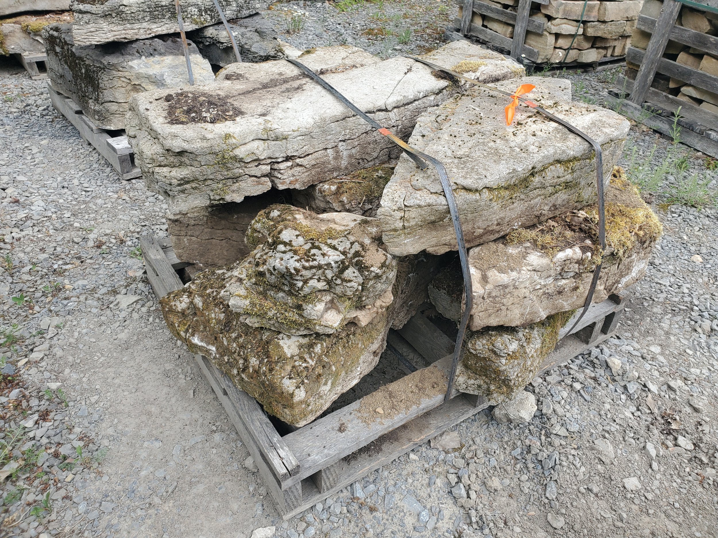 Large old rocks stacked on wooden pallets and tied with metal straps in an outdoor setting.