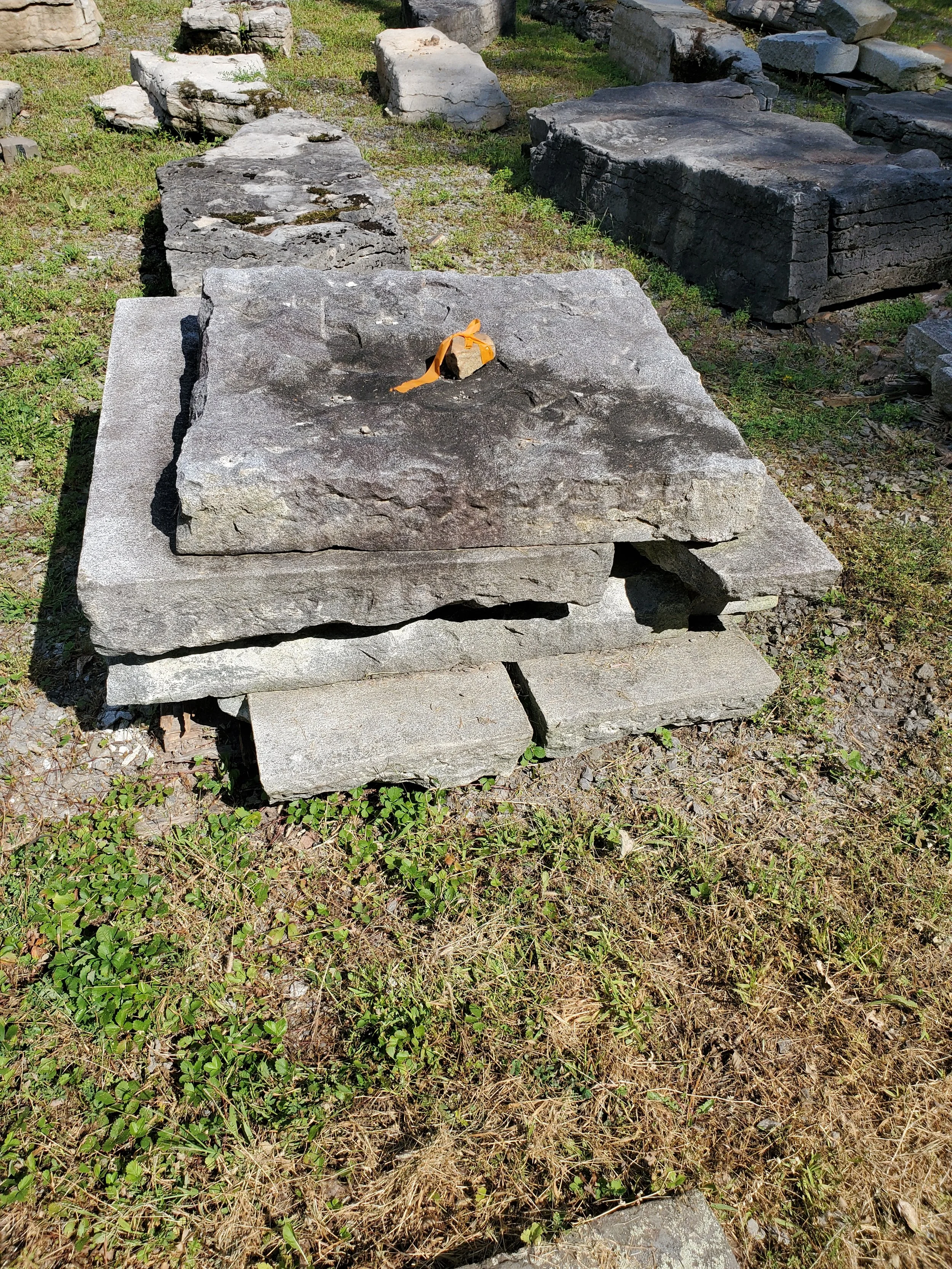 Stacked flat stones on grass, with a small, tied orange ribbon on top