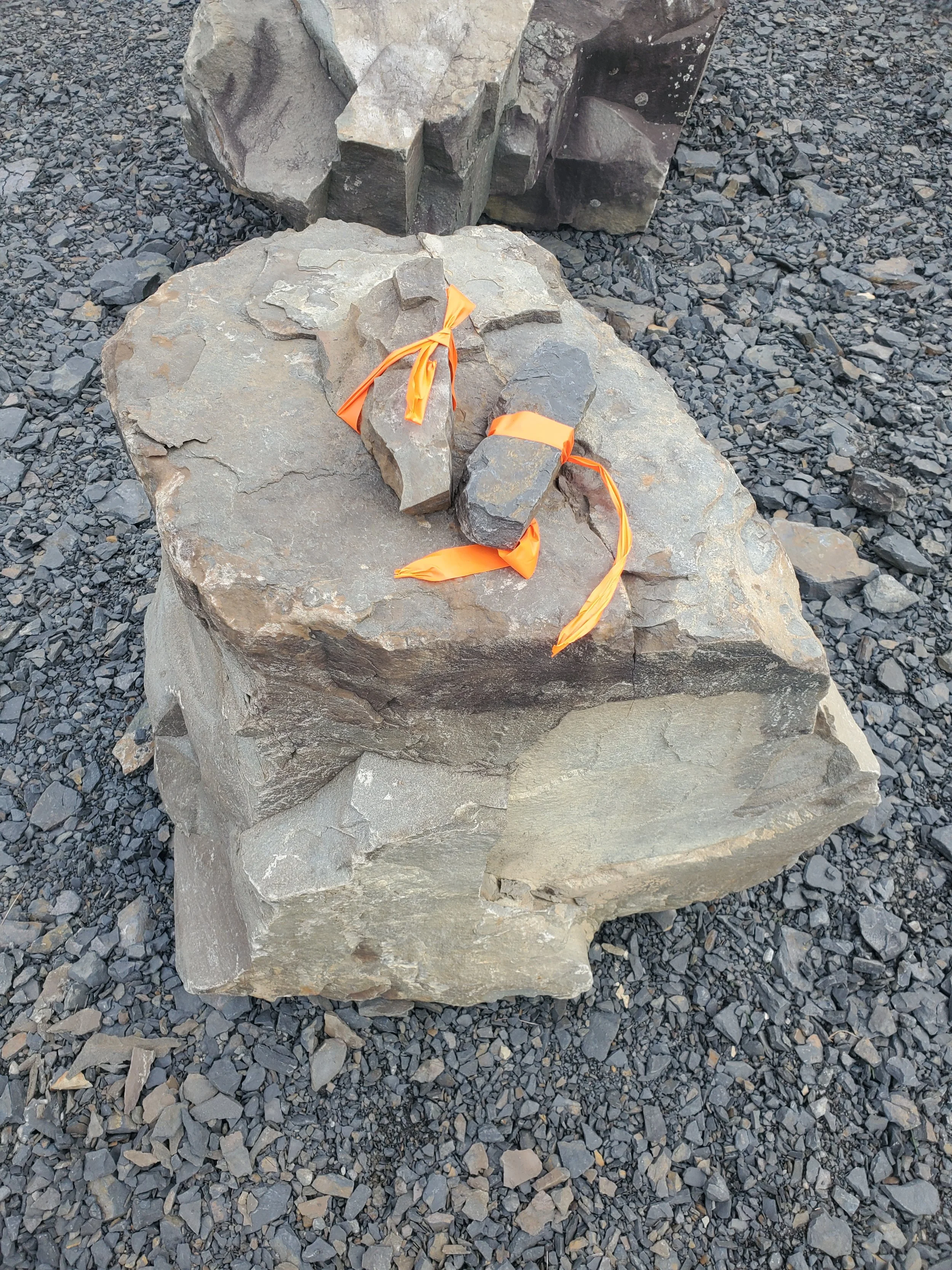 Large beige and dark gray rocks on a gravel surface, with orange ribbons tied around smaller rocks on top.