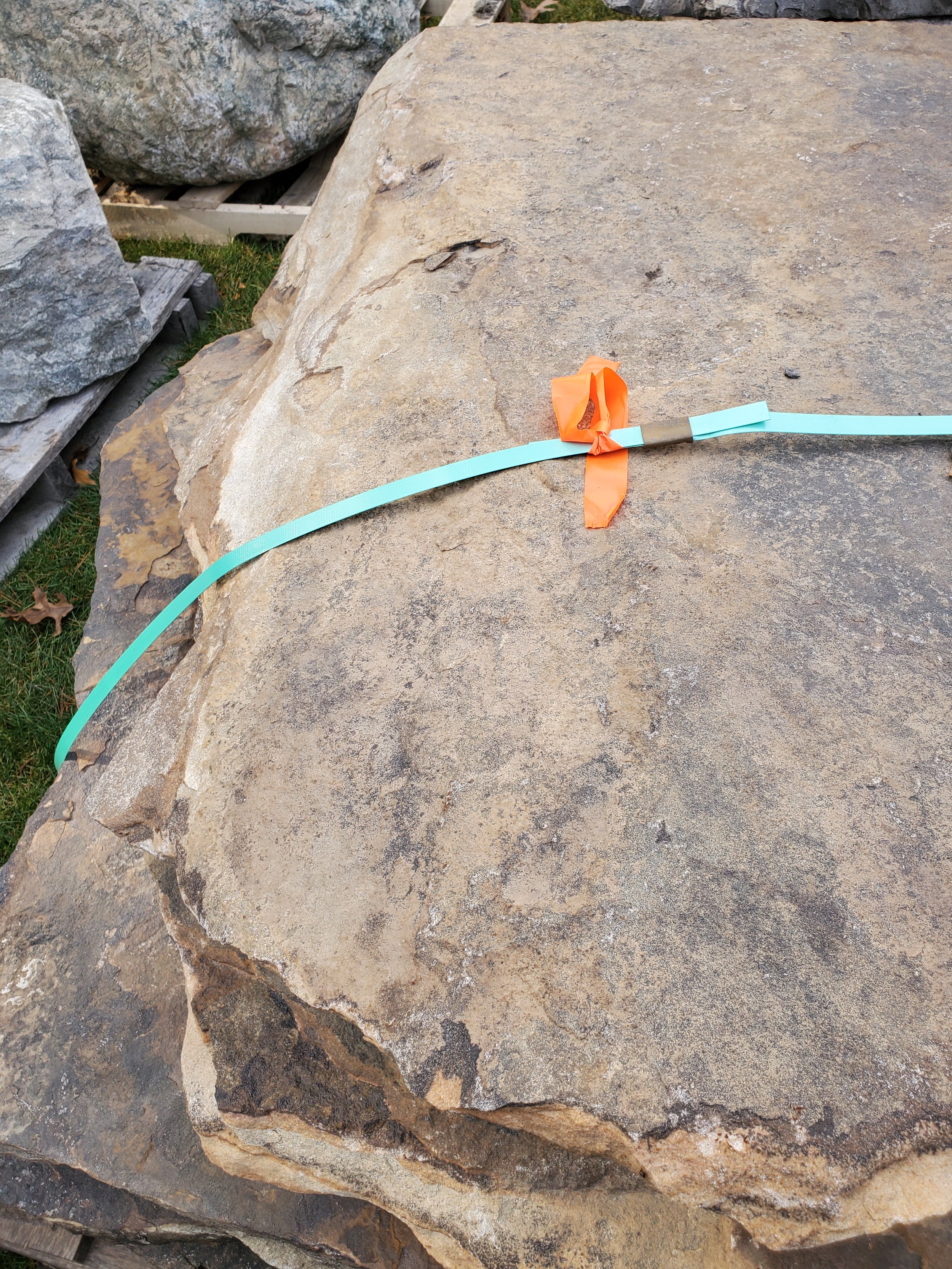 A large flat stone with a blue and orange string tied around it, with the string forming a knot in the center.