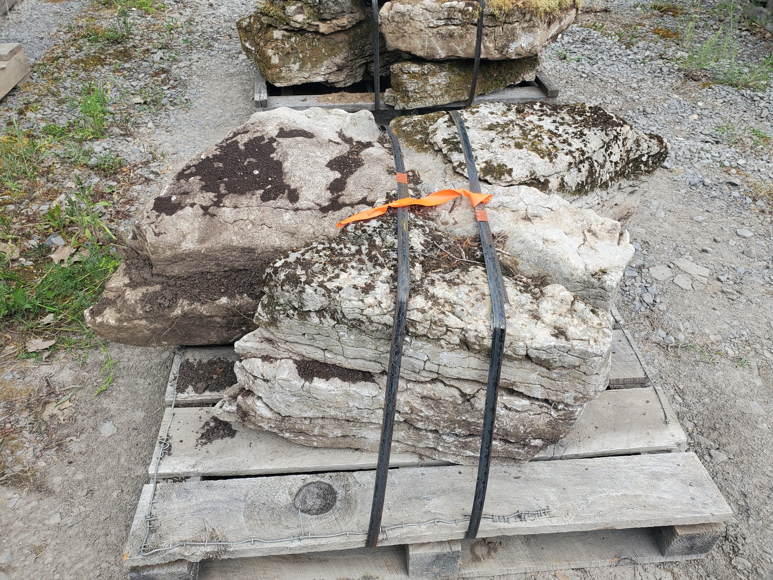 Stacked large rocks secured with black straps and orange ribbon on a wooden pallet outdoors.