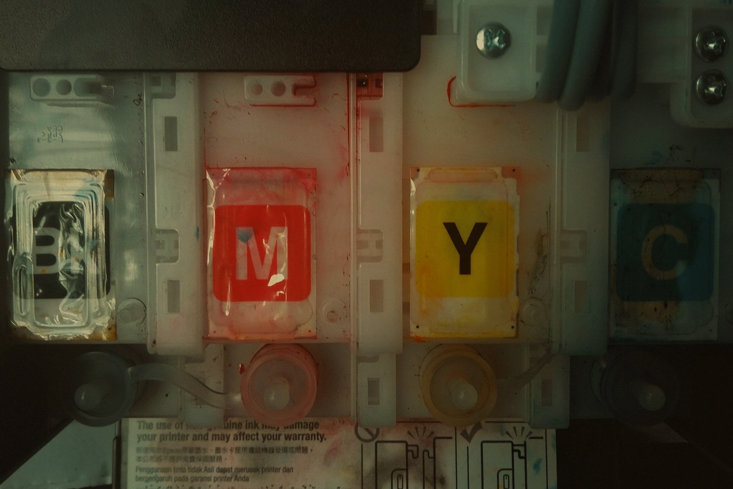 Close-up of a printer ink cartridge set with ink labels 'M', 'Y', and 'C' in red, yellow, and blue colors respectively.