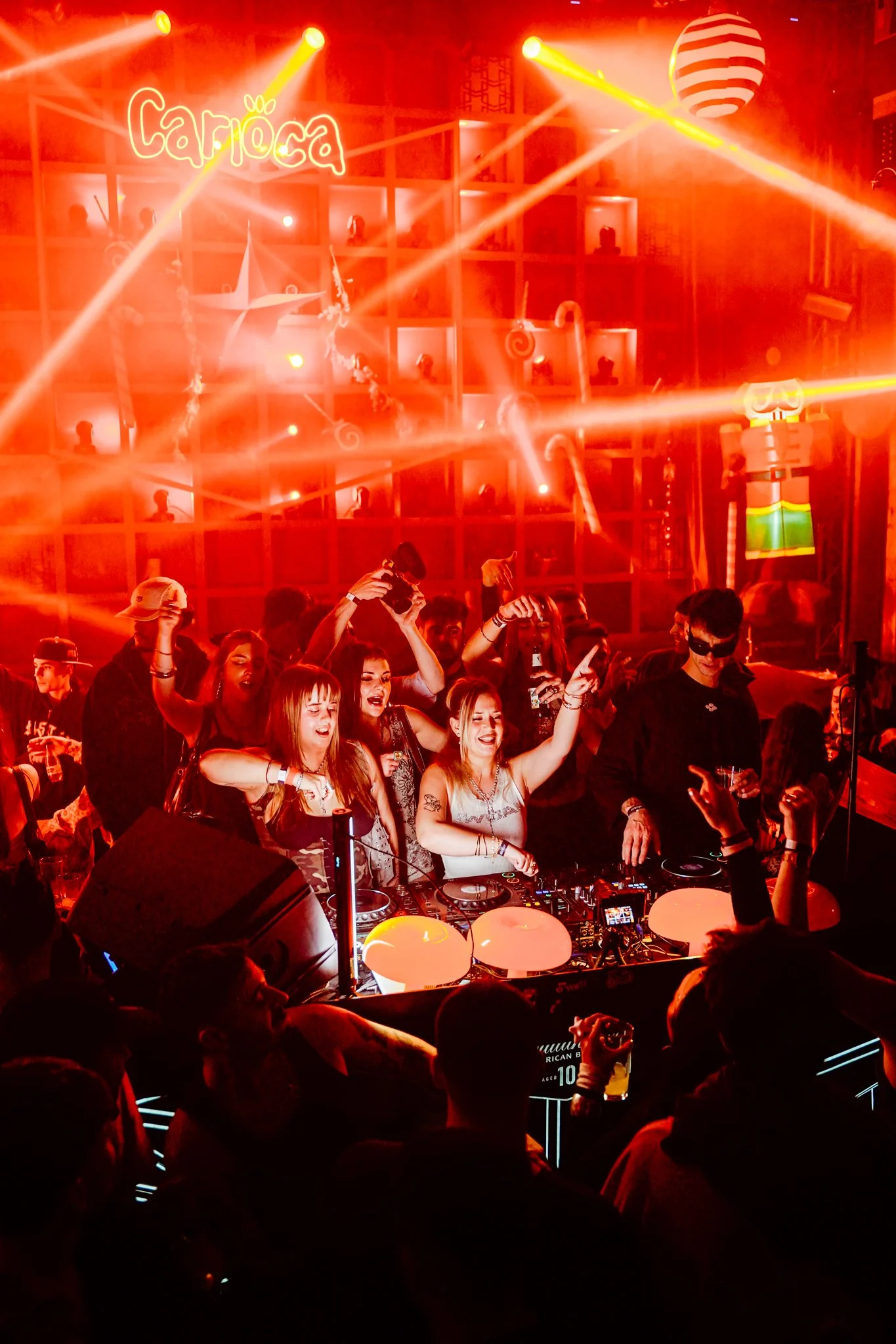 Crowd dancing and enjoying music at a vibrant nightclub with colorful lights and a DJ setup.