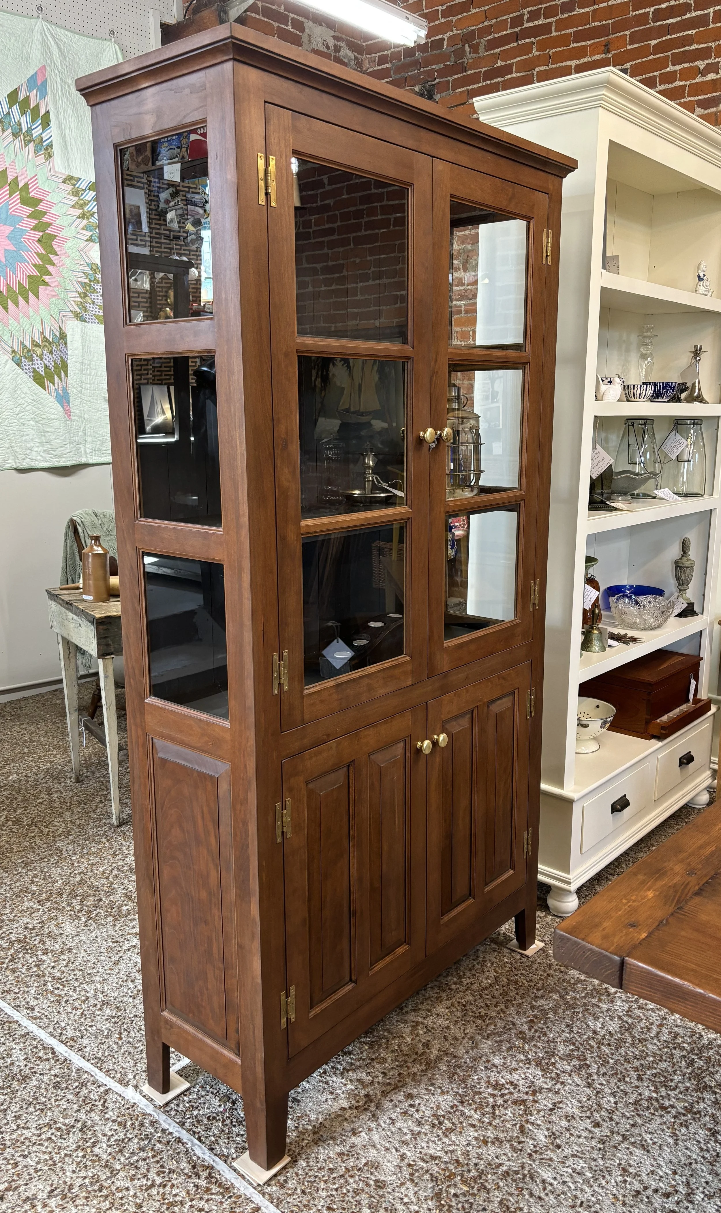 A tall wooden display cabinet with glass doors and brass hinges, standing in an indoor store environment.