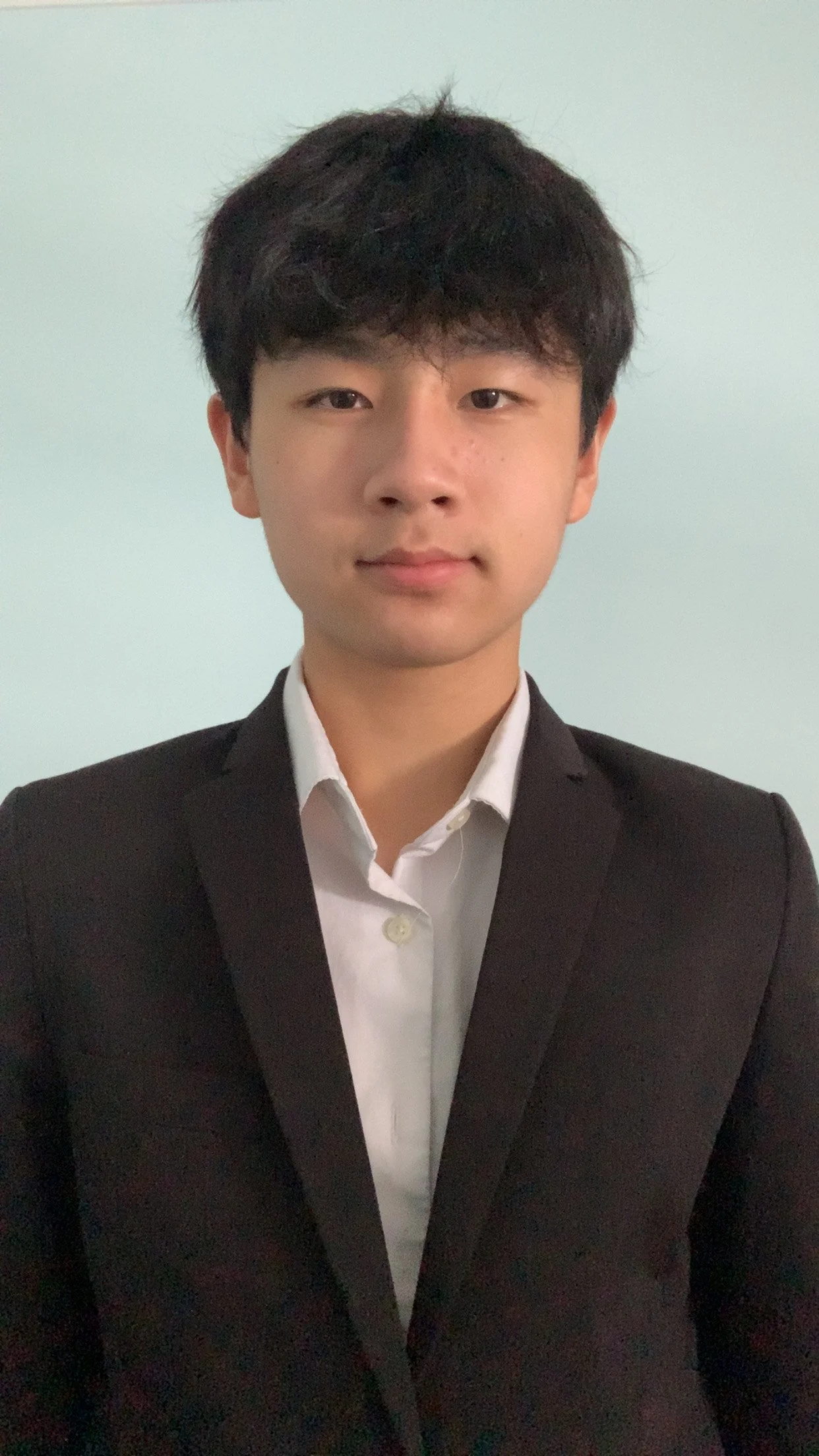Young man in a black suit and white shirt taking a selfie.