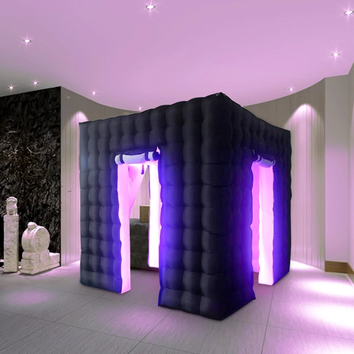 Black inflatable photo booth enclosure with purple lighting inside, set up indoors with a pink ceiling and white walls.