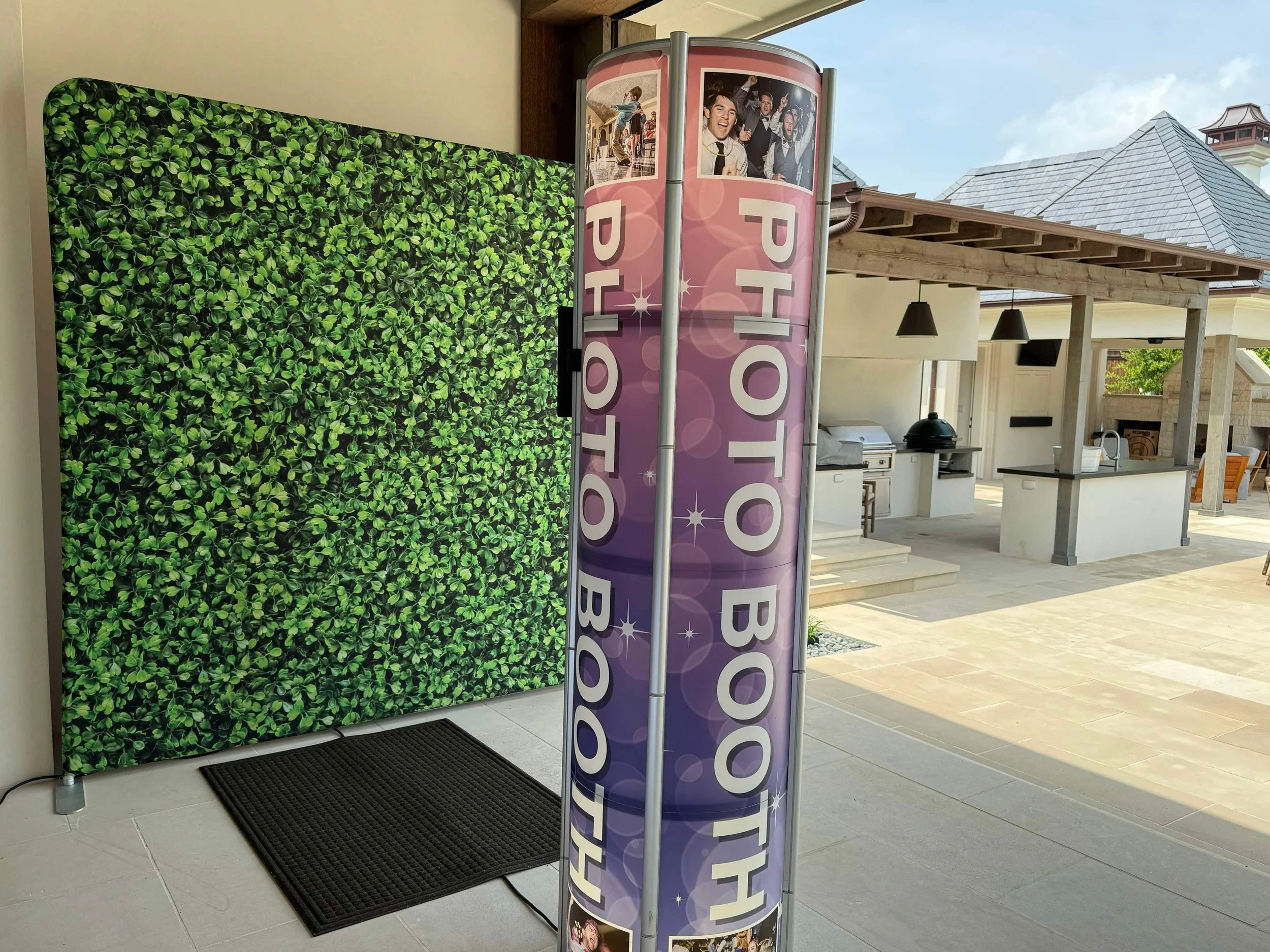 A tower style photo booth with leafy green printed backdrop