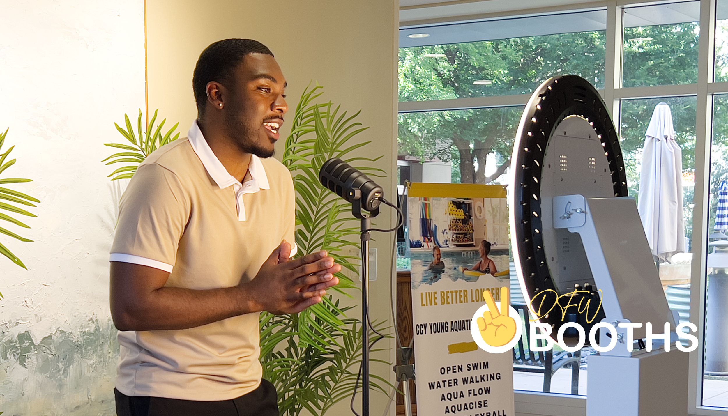 A young Black man in a tan polo shirt actively speaking and gesturing into a dynamic microphone at a professional video testimonial activation booth.
