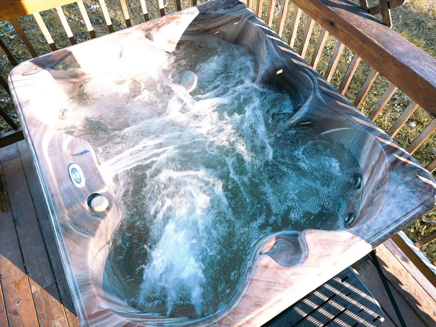 A hot tub on a wooden deck outdoors with bubbling water and built-in jets.