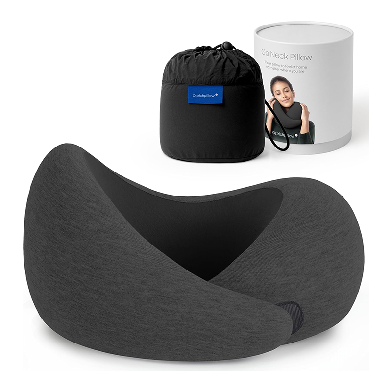 A black neck pillow in front of a cylindrical packaging box showing a woman resting her head on a pillow, and a black drawstring storage bag with a label, all placed on a white background.