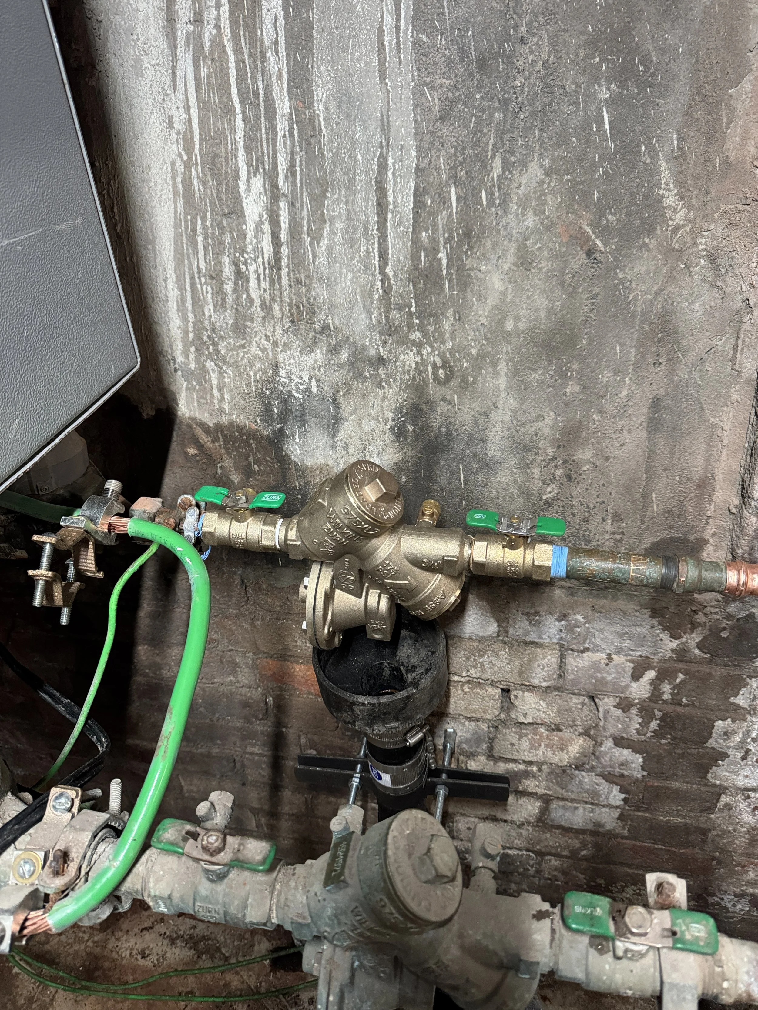 Plumbing pipes, valves, and fittings installed against a brick wall.