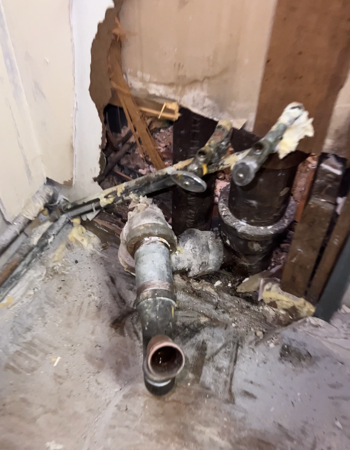 Construction or plumbing work in progress, showing exposed pipes and unfinished wall with drywall and wood framing.