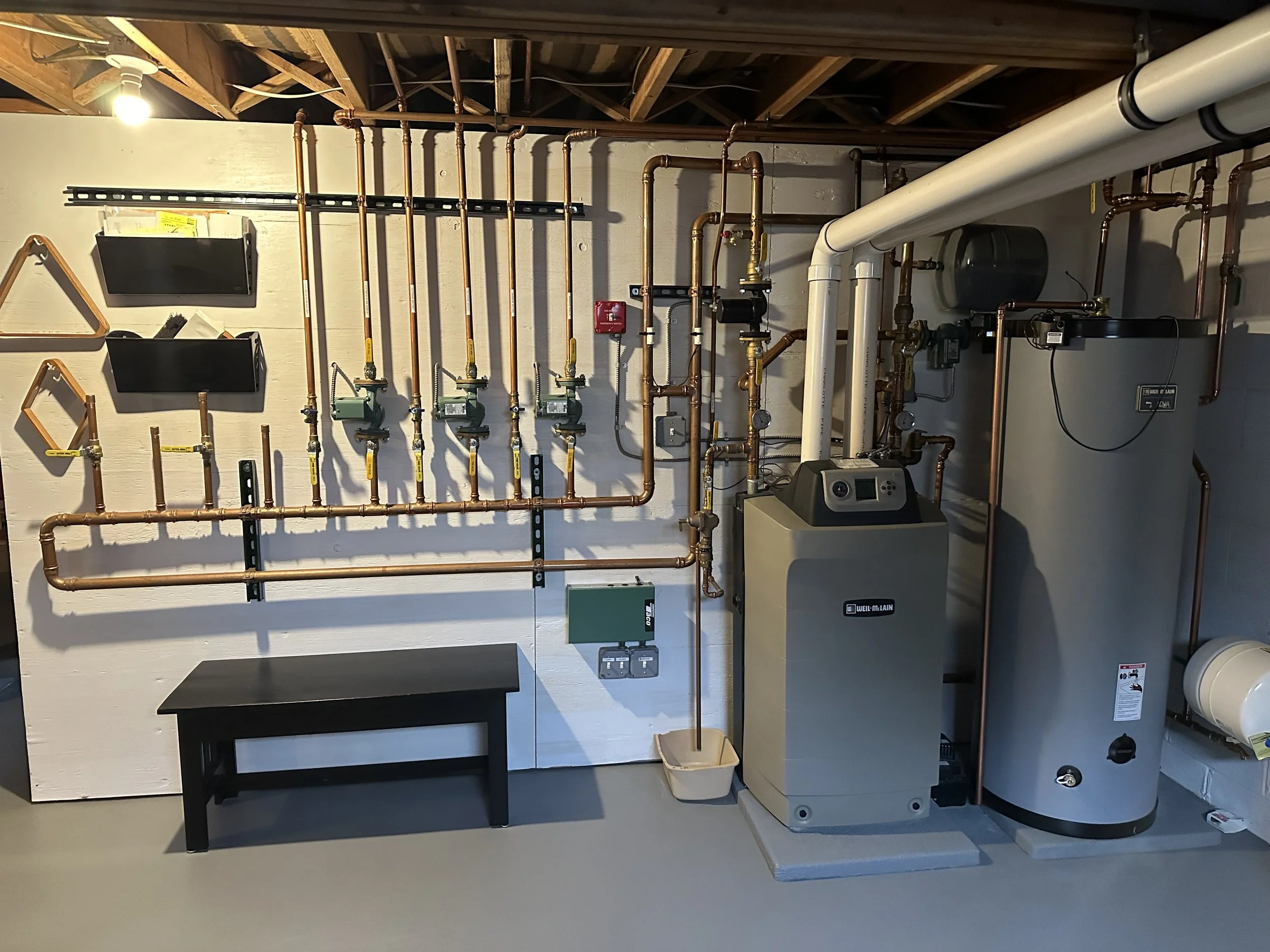 A utility room with copper piping, plumbing components, and a water heater system.