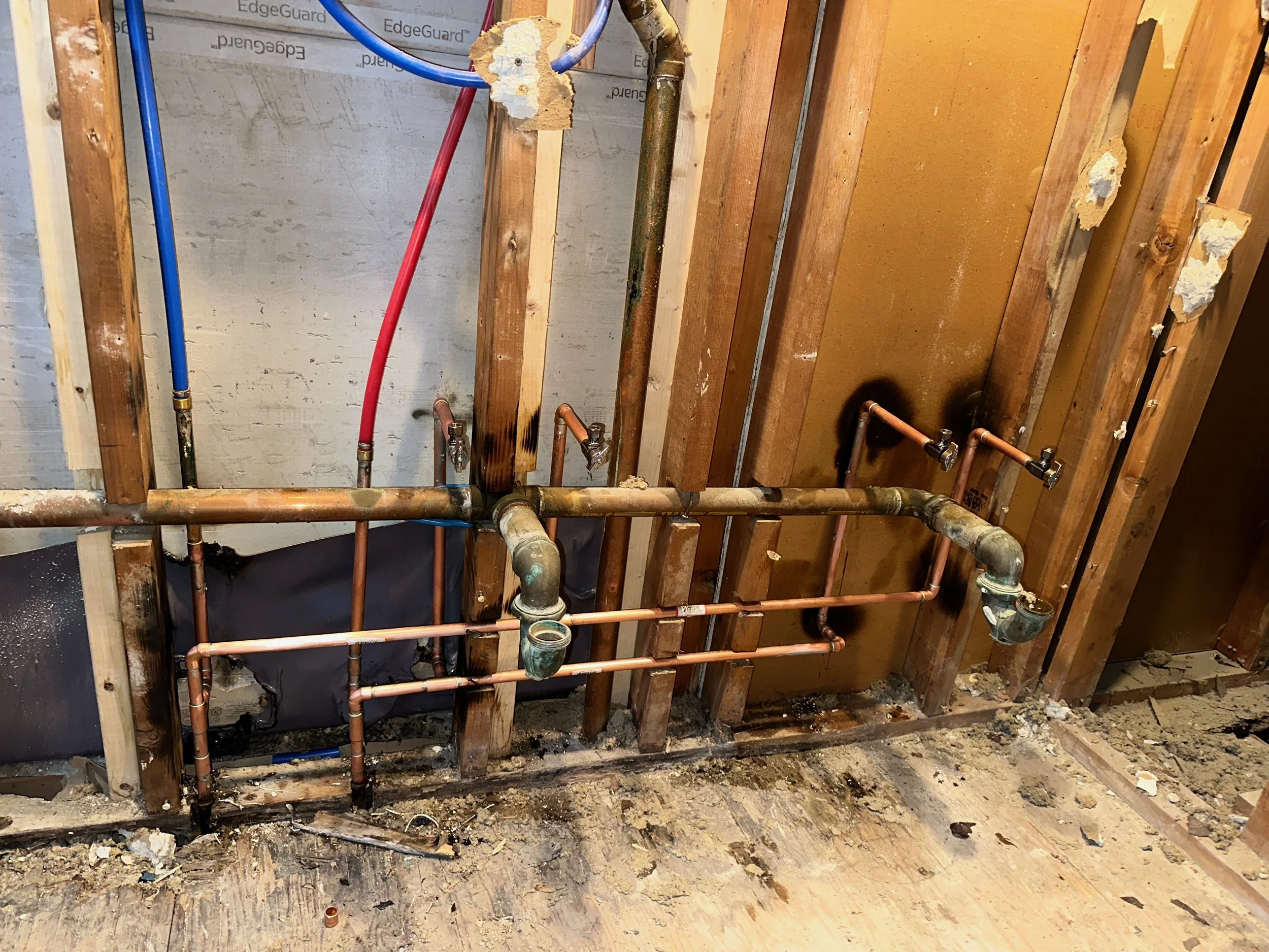 Open wall with exposed copper pipes, water supply lines, and framing for plumbing installation in a construction site.