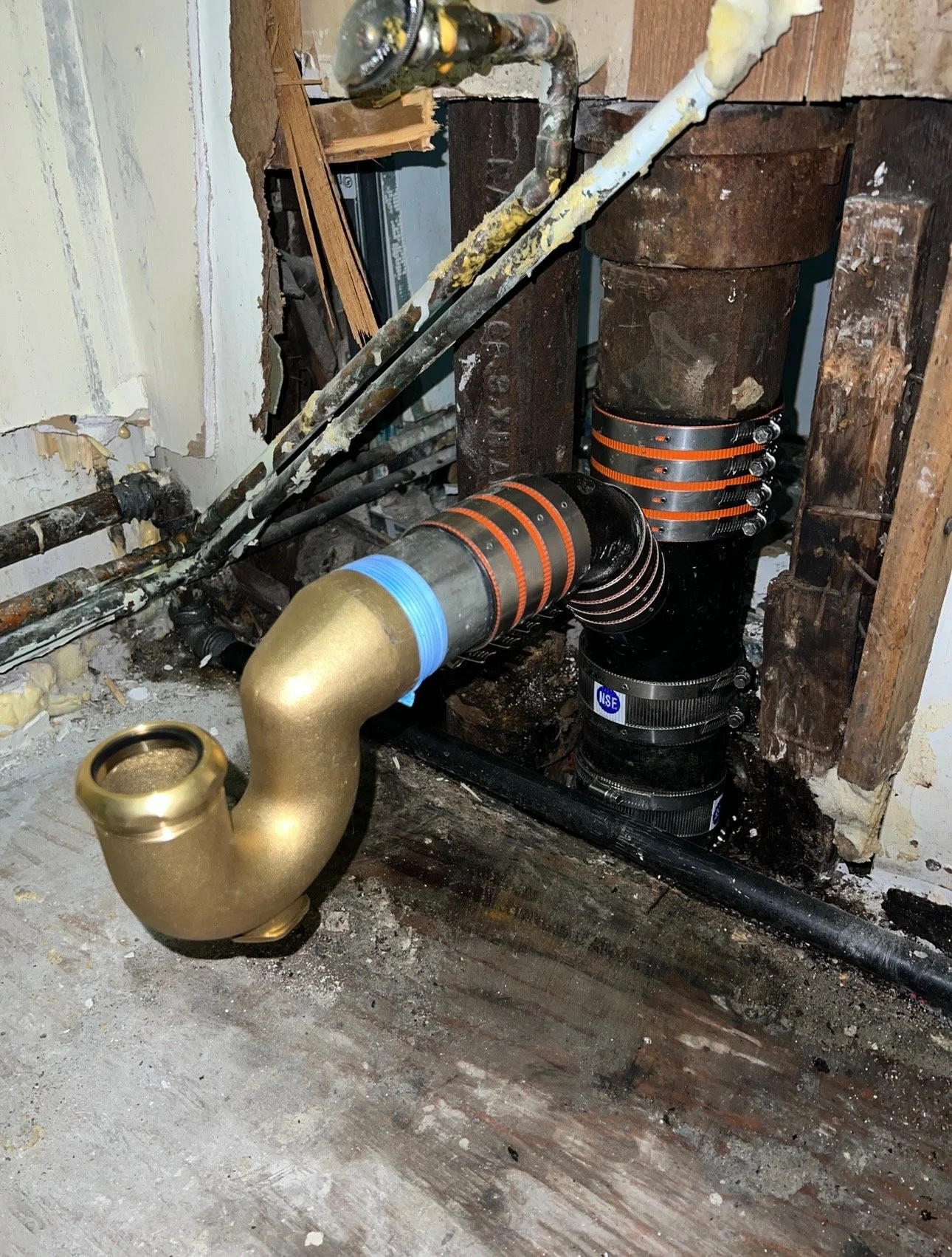 Plumbing pipes connected to a sump pump in a basement wall with exposed studs and wall studs.